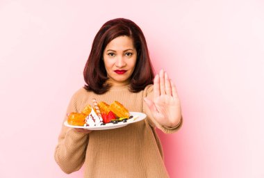 Orta yaşlı Latin bir kadın, elinde bir waffle tutarken elini uzatmış, dur işareti göstererek seni engelliyor..