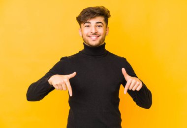 Sarı arka planda izole edilmiş genç bir Arap, parmakları aşağıda, olumlu bir his var..