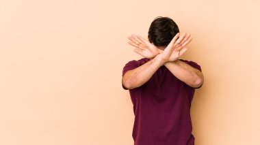 Bej arka planda izole edilmiş genç adam iki kolu çapraz tutuyor, inkar kavramı.