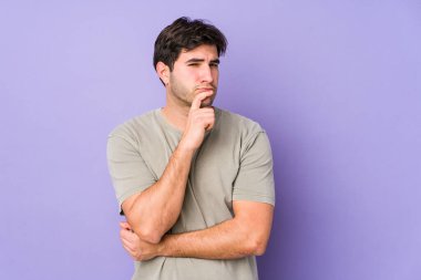 Genç adam mor arka planda izole edilmiş düşünüyor, yukarı bakıyor, yansıtıyor, düşünüyor, bir fantezi kuruyor..