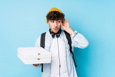 Elinde pizza tutan genç bir Arap öğrenci bir dedikoduyu dinlemeye çalışıyor..