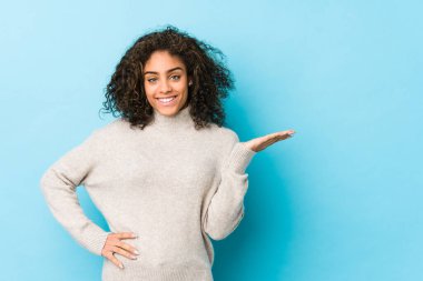 Genç Afro-Amerikalı kıvırcık saçlı kadın bir avuç içinde fotokopi alanı gösteriyor ve belinde bir el daha tutuyor..