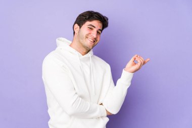 Mor arka planda izole edilmiş genç adam işaret parmağıyla işaret ederek gülümsüyor..