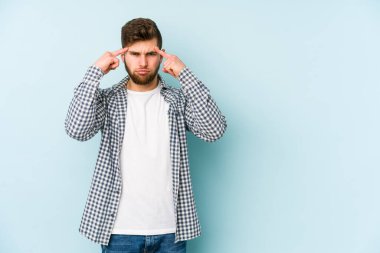 Kafkasyalı genç adam mavi arka planda izole edilmiş bir göreve odaklanmış, parmaklarını işaret ediyor..