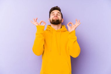 Mor arka planda izole edilmiş genç beyaz adam sıkı çalışma gününden sonra rahatlıyor. Yoga yapıyor..