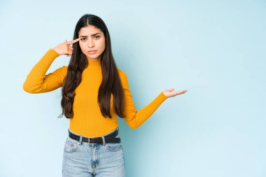 Genç Hintli bir kadın mavi arka planda izole edilmiş ve elinde bir ürün tutuyor..