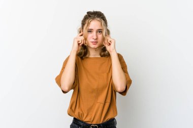Beyaz arka plandaki genç beyaz kadın parmaklarıyla kulaklarını kapatıyor, gürültülü bir ortam yüzünden stresli ve çaresiz..