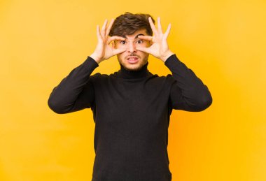 Sarı arka planda izole edilmiş genç bir Arap, başarı fırsatı bulmak için gözlerini açık tutuyor..