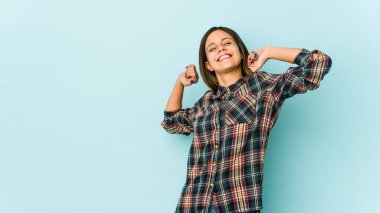 Mavi arka planda izole edilmiş genç bir kadın. Kollarını uzatıyor, rahat duruyor..