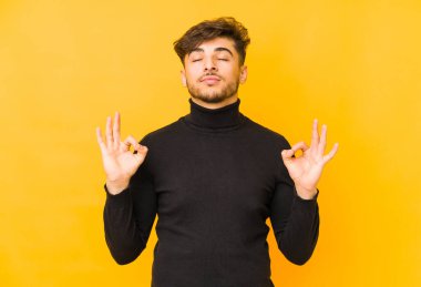 Sarı arka planda izole edilmiş genç bir Arap adam yoğun bir günün ardından rahatlıyor, yoga yapıyor..