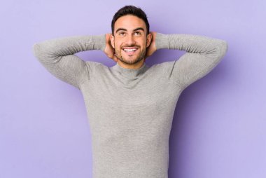 Mor arka planda izole olmuş genç beyaz bir adam kendini güvende hissediyor, elleri başının arkasında..