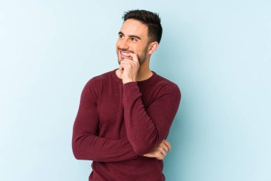 Mavi arka planda izole edilmiş genç beyaz adam rahatlamış bir şeyin fotokopi odasına baktığını düşünüyor..