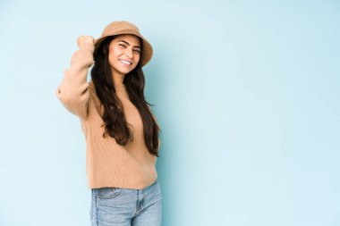 Mavi arka planda izole edilmiş bir şapka takan genç Hintli kadın zafer, tutku ve coşkuyu kutluyor, mutlu bir ifade..