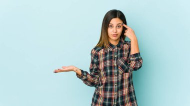Mavi arka planda izole edilmiş genç bir kadın işaret parmağıyla bir hayal kırıklığı gösteriyor..