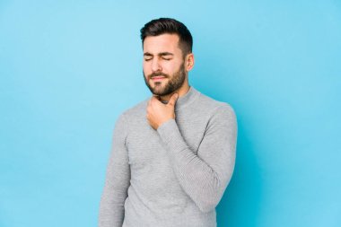 Mavi arka planda yaşayan beyaz bir genç, virüs veya enfeksiyon yüzünden boğazında ağrı hissediyor..