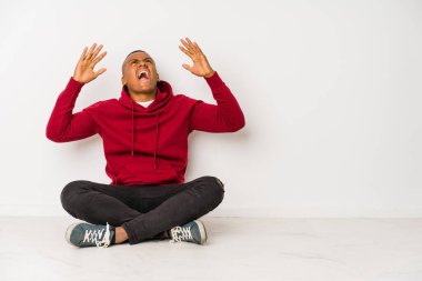 Yerde tek başına oturan genç latin adam gökyüzüne haykırıyor, yukarı bakıyor, hayal kırıklığına uğramış..