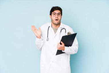 Genç doktor mavi arka planda izole edildi. Şaşırdı ve şok oldu..