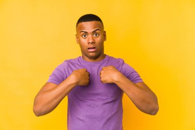 Sarı arka planda izole edilmiş genç latin adam parmağını göstererek şaşırdı, geniş bir gülümsemeyle..