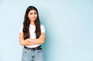 Mavi arka plandaki genç Hintli kadın iğneleyici bir ifadeyle kameraya bakarken mutsuz oluyor..