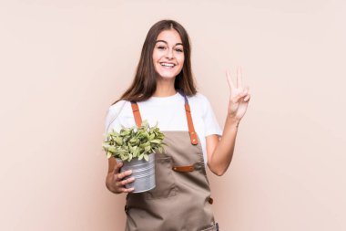 Genç bahçıvan Kafkas kadın elinde bir bitki tutuyor. İki numarayı parmaklarıyla gösteriyor..