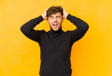 Sarı arka planda izole edilmiş genç bir Arap adam ellerini başının üstünde tutarak neşeyle gülüyor. Mutluluk kavramı.