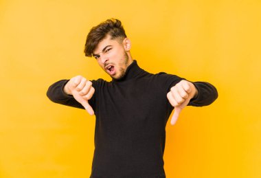 Sarı arka planda izole edilmiş genç bir Arap, baş parmağını aşağı gösteriyor ve hoşlanmadığını ifade ediyor..