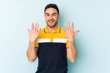 Mavi arka planda izole edilmiş genç beyaz adam on numarayı elleriyle gösteriyor..