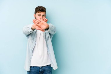 Kafkasyalı genç adam mavi arka planda izole edilmiş bir şekilde inkar hareketi yapıyor.