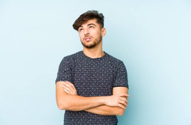 Mavi arka planda izole edilmiş genç bir Arap adam tekrarlanan bir görevden yoruldu.