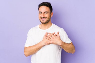 Mor arka planda izole edilmiş beyaz bir genç, dost bir ifadeye sahip, avuçlarını göğsüne bastırıyor. Aşk konsepti.
