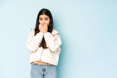 Mavi arka planda genç Hintli kadın tırnaklarını yiyor, gergin ve çok endişeli..