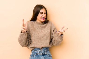 Beyaz tenli genç bir kadın bej arka planda neşeli bir şekilde gülüyor. Mutluluk kavramı.