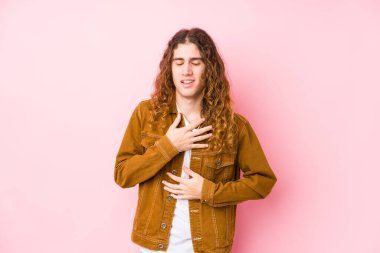 Uzun saçlı genç adam yalnız gülüyor ve ellerini karnının üstünde tutarak eğleniyor..