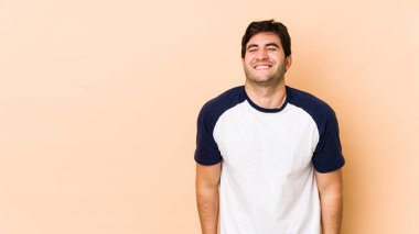 Bej arka planda izole edilmiş genç adam gülüyor ve gözlerini kapıyor, rahatlamış ve mutlu hissediyor..