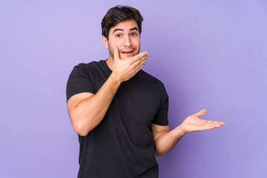 Mor arka planda izole edilmiş genç bir adam, bir avuç içinde fotokopi alanı tutar, el üstünde yanak tutar. Şaşırmış ve mutlu..