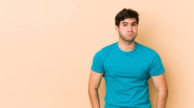 Bej arka planda izole edilmiş genç adamın yanakları şişiyor, yorgun bir ifadesi var. Yüz ifadesi kavramı.