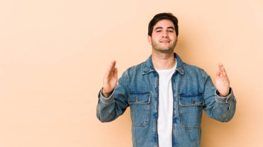 Bej arka planda izole edilmiş genç bir adam işaret parmaklarıyla küçük bir şey tutuyor, gülümsüyor ve kendinden emin..