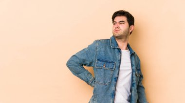 Bej arka planda izole edilmiş genç bir adam sırt ağrısı çekiyor..