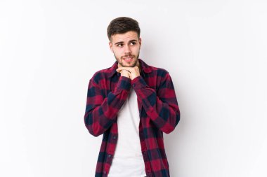 Beyaz arka planda poz veren beyaz tenli genç adam ellerini çenesinin altında tutuyor ve mutlu bir şekilde yan tarafa bakıyor..