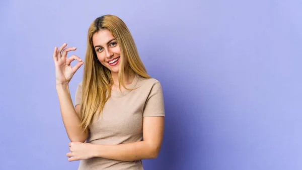 Young Blonde Woman Isolated Purple Background Winks Eye Holds Okay — Stock Photo, Image