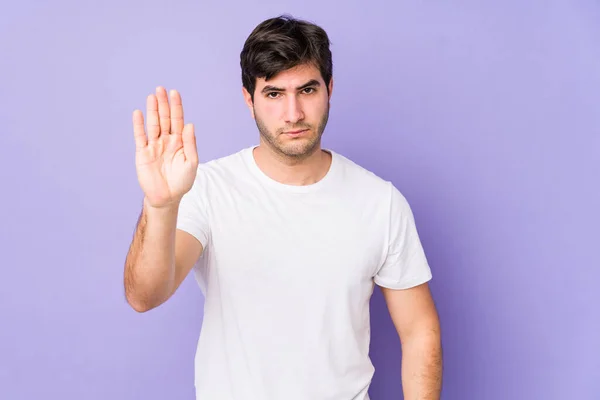 紫色の背景で隔離された若い男が停止標識を示す手を伸ばしてあなたを防ぎます — ストック写真