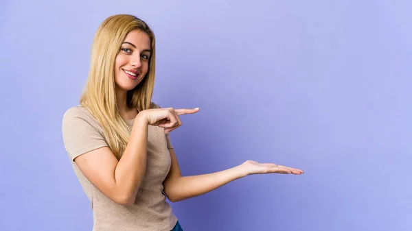 Jovem Loira Isolada Fundo Roxo Animado Segurando Espaço Cópia Palma — Fotografia de Stock