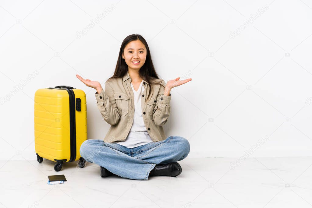 Young chinese traveler woman sitting holding a boarding passes makes scale with arms, feels happy and confident.