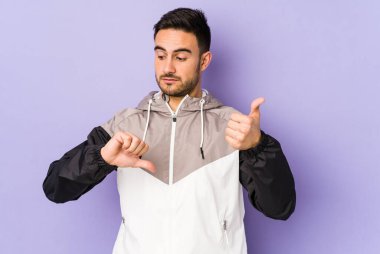 Mor arka planda izole edilmiş genç beyaz adam baş parmağını kaldırıyor ve baş parmağını aşağı gösteriyor, zor seçim kavramı.
