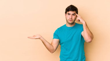 Bej arka planda izole edilmiş genç bir adam elinde bir ürün tutuyor..