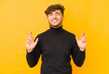 Sarı arka planda izole edilmiş genç bir Arap adam şans dilemek için şans diliyor.