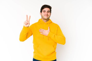 Beyaz arka planda yaşayan genç bir adam yemin ediyor, elini göğsüne koyuyor..