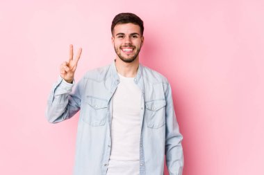 Beyaz arka planda poz veren beyaz tenli genç iş adamı zafer işareti gösteriyor ve gülümsüyor..