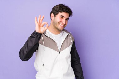 Mor arka planda izole edilmiş genç adam neşeli ve kendinden emin, iyi bir hareket gösteriyor..