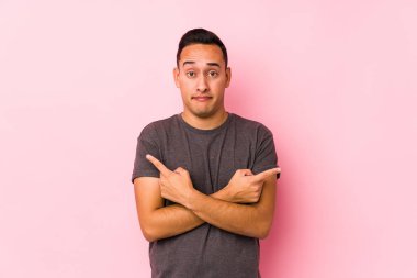 Pembe arka planda poz veren yog latin adam iki seçenek arasında seçim yapmaya çalışıyor..